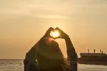 Hands forming heart shape with sunset silhouette
